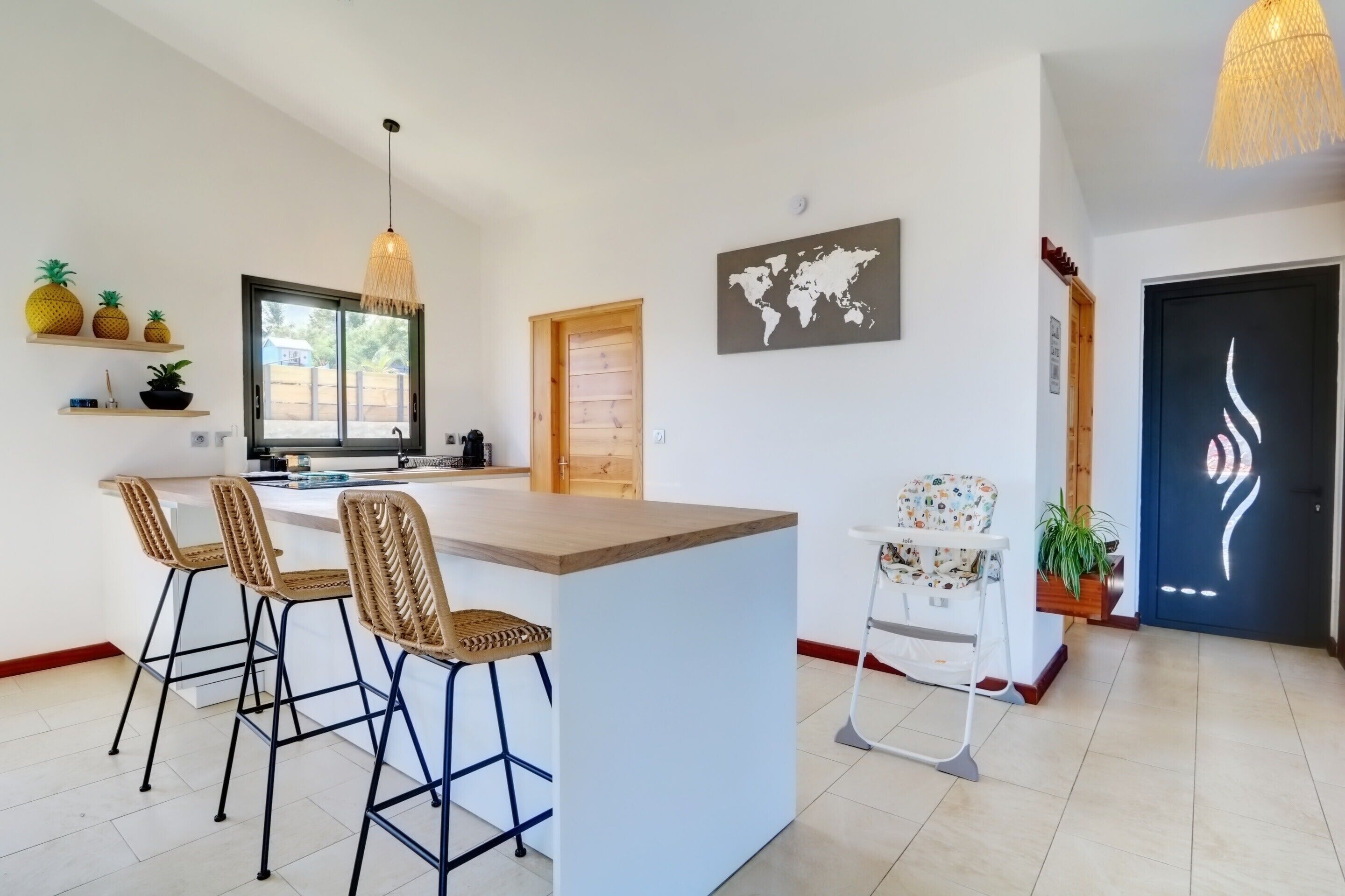 Una cucina moderna con isola centrale, sgabelli da bar, lampadario a sospensione, una mappa del mondo e una porta dal design particolare.