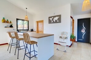A modern kitchen with a central island, bar stools, a hanging light fixture, a world map, and a door with a unique design. - Villa Aïna - Vue mer - Piscine (Saint-Leu)