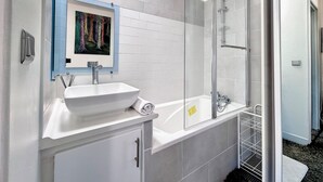 Ein modernes Badezimmer mit einem weißen Waschbecken, einem großen Spiegel und einer Duschkabine aus Glas.