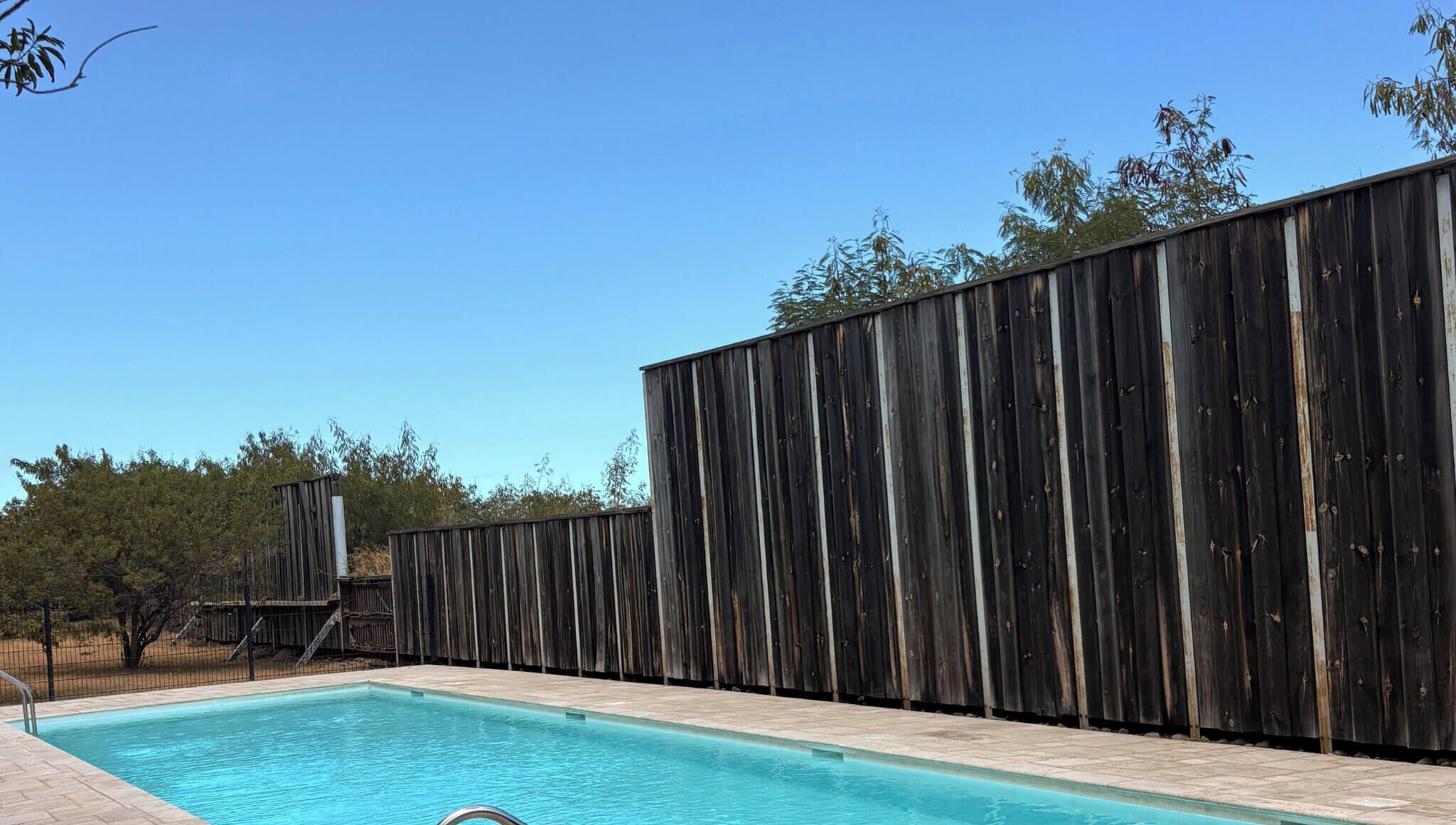 A swimming pool with a wooden fence and a clear blue sky.