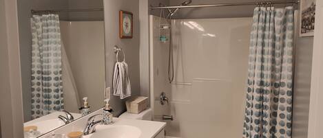 Een badkamer met een wit wastafel, toilet, douche met gordijn en een spiegel met verlichting erboven.