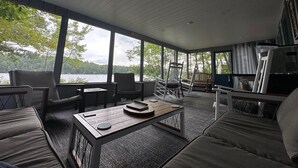 Ruime binnenruimte met een groot raam met uitzicht op een wateroppervlak, ingericht met een bank, stoelen en een tafel.