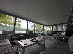 A spacious indoor area with a large window overlooking a body of water, furnished with a sofa, chairs, and a table. - Sebago Lake Waterfront Cottage Sandy Beach Boats Frye Island Maine Ferry Tale (Frye Island)