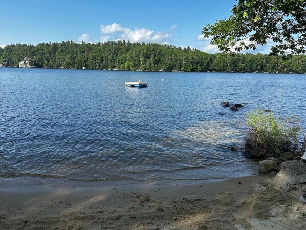 A calm lake with a small boat, a sandy beach, and a forested shoreline. - Sebago Lake Waterfront Cottage Sandy Beach Boats Frye Island Maine Ferry Tale (Frye Island)
