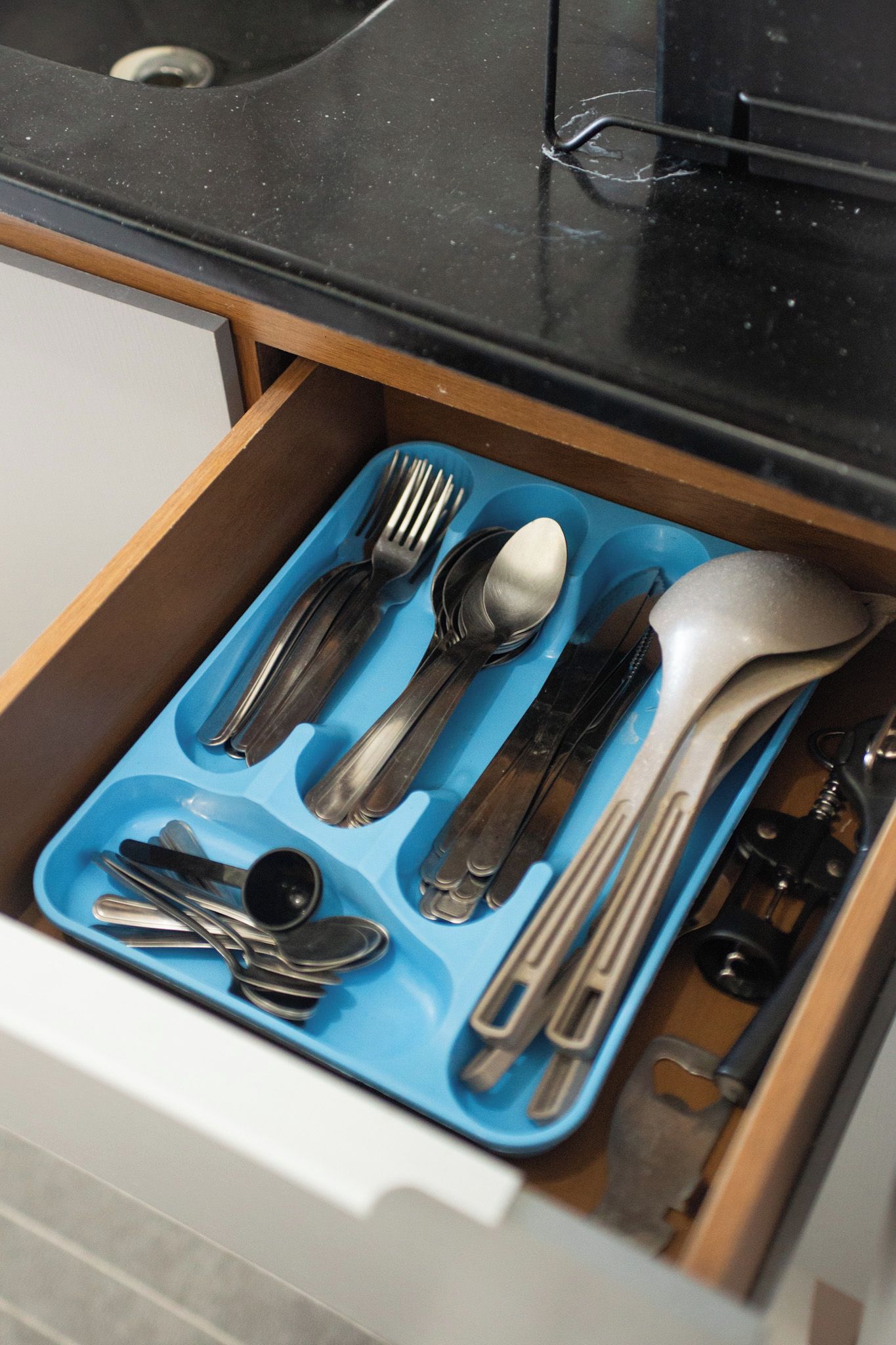 A drawer with a blue utensil organizer containing forks, spoons, and knives.