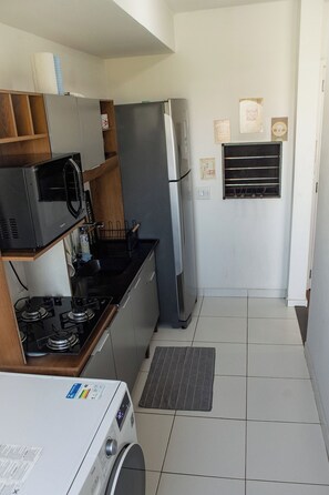 A compact kitchen with a gas stove, microwave, refrigerator, and a washing machine. - Tricolor Area! Cozy apartment next to Grêmio Arena, near the airport. (Porto Alegre)