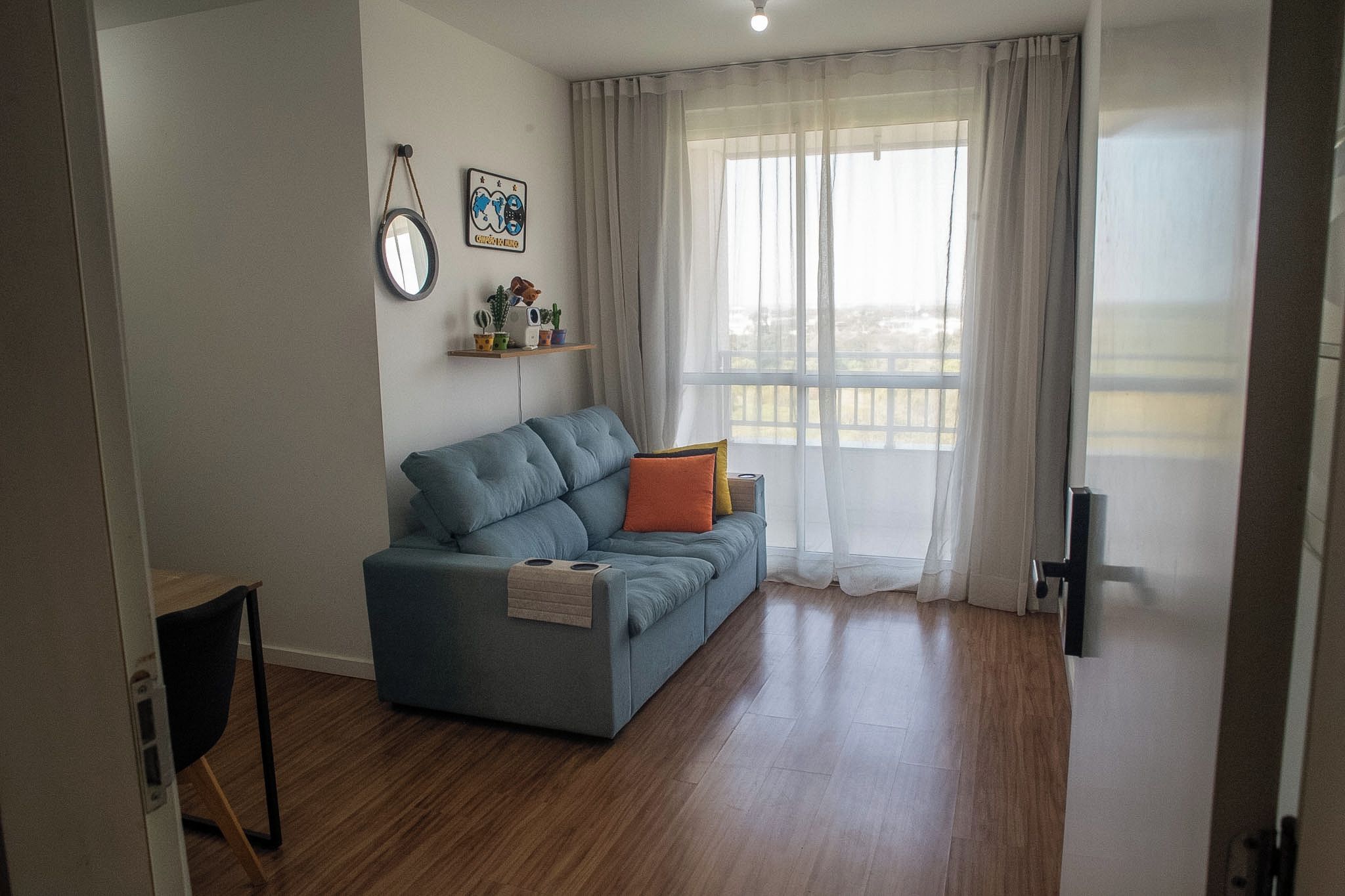 A living room with a blue sofa, a small table, and a window with sheer curtains.