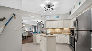A modern kitchen with white cabinets, a central island, a stainless steel refrigerator, and a ceiling fan with lights. - Windward Pointe 3 Bed 2 Bath - Sleeps 10.  Free Daily Activities! (Orange Beach)