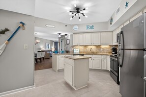 A modern kitchen with white cabinets, a central island, a stainless steel refrigerator, and a ceiling fan with lights. - Windward Pointe 3 Bed 2 Bath - Sleeps 10.  Free Daily Activities! (Orange Beach)
