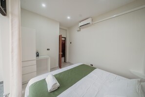 Una habitación de hotel con una cama, un escritorio, un espejo y un equipo de aire acondicionado.