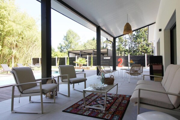 A covered outdoor seating area with chairs and a coffee table, a pool in the background, and a large number '2' sign. - Villa J - GUJAN MESTRAS (GUJAN MESTRAS)