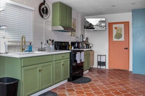 A kitchen with green cabinets, a black oven, a sink with a gold faucet, and a small trash bin.