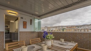 En uteservering med ett bord för två personer, en krukväxt och utsikt över staden.