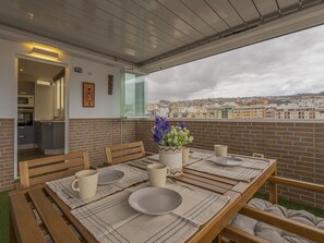 Ein Essbereich im Freien mit einem Tisch für zwei Personen, einem Blumentopf und Blick auf die Stadt.