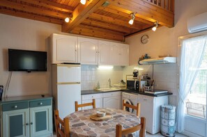 A compact kitchen with white cabinets, a sink, a microwave, and a dining table with chairs. - Riboleys - Maison climatisée à 550m de la mer (Vias)