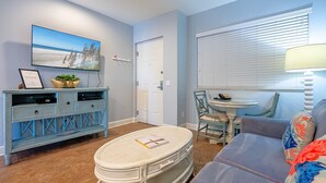 A living room with a television, a small table with chairs, a sofa, and a ceiling fan. - Harbour House #315 - "Coastal Cabana" (Fort Myers Beach)