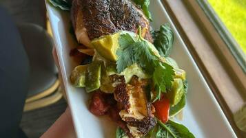 A rectangular white plate with a grilled meat dish, avocado, and greens, held by a person.