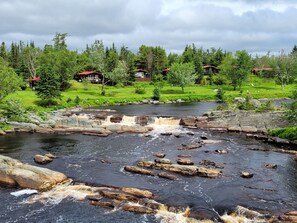 A river with a waterfall, surrounded by green trees and houses with red roofs. - Deluxe Accessible King Chalet with River View Deck (Liscomb)