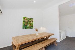 A room with a wooden table and benches, a white brick wall, and a green painting.