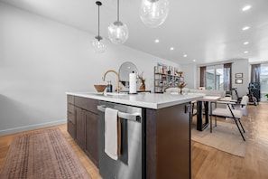 A modern kitchen with a central island, stainless steel appliances, pendant lighting, and a dining area with a table and chairs. - Roam Retreat Near Snowbasin R5931 | Pool | Hot Tub (Mountain Green)