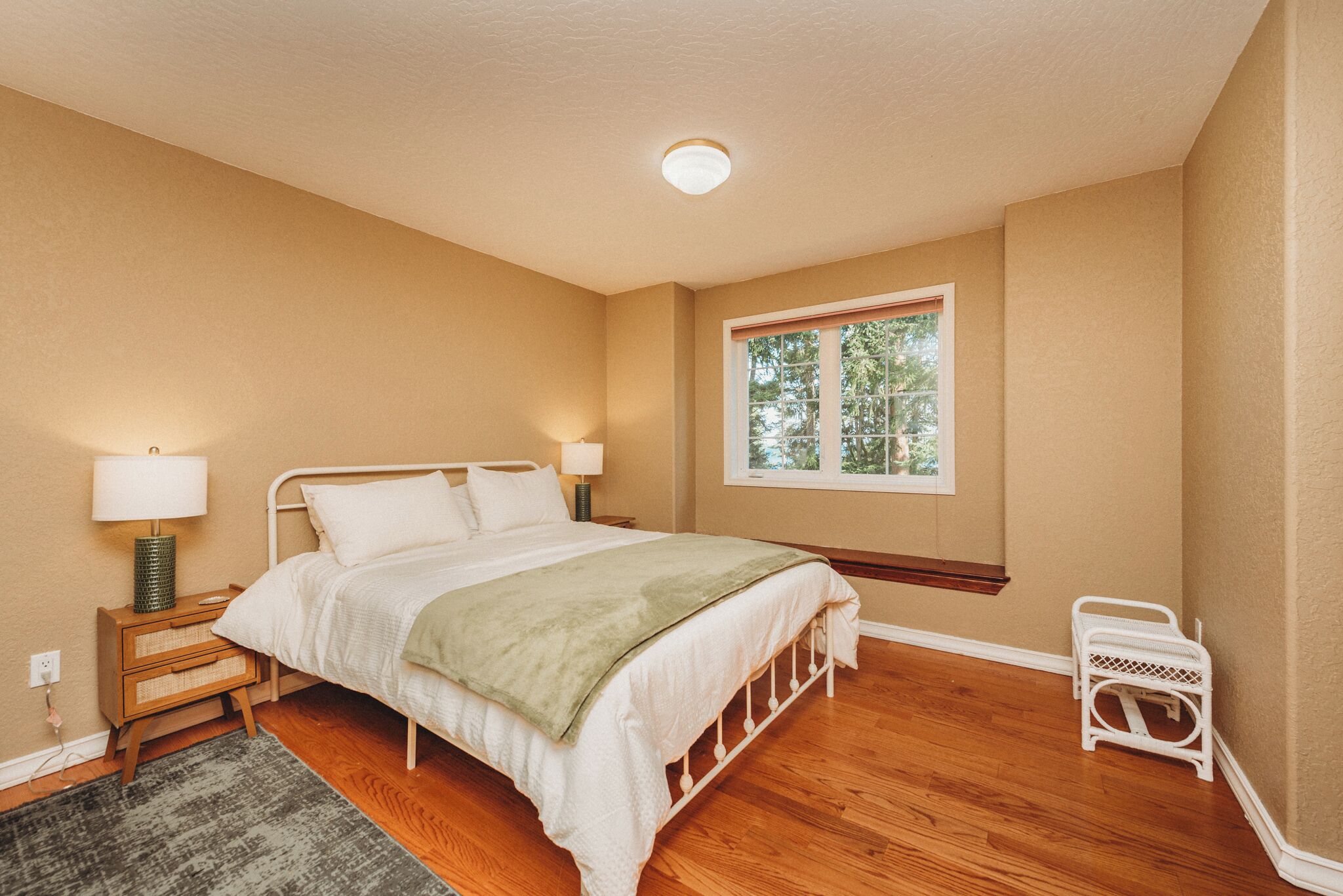 A bedroom with a bed, bedside tables, a window, and a nightstand.