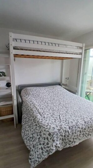 A bunk bed with a patterned bedspread, a white headboard, and a window with a view. - Studio with parking Dinard center (Dinard)