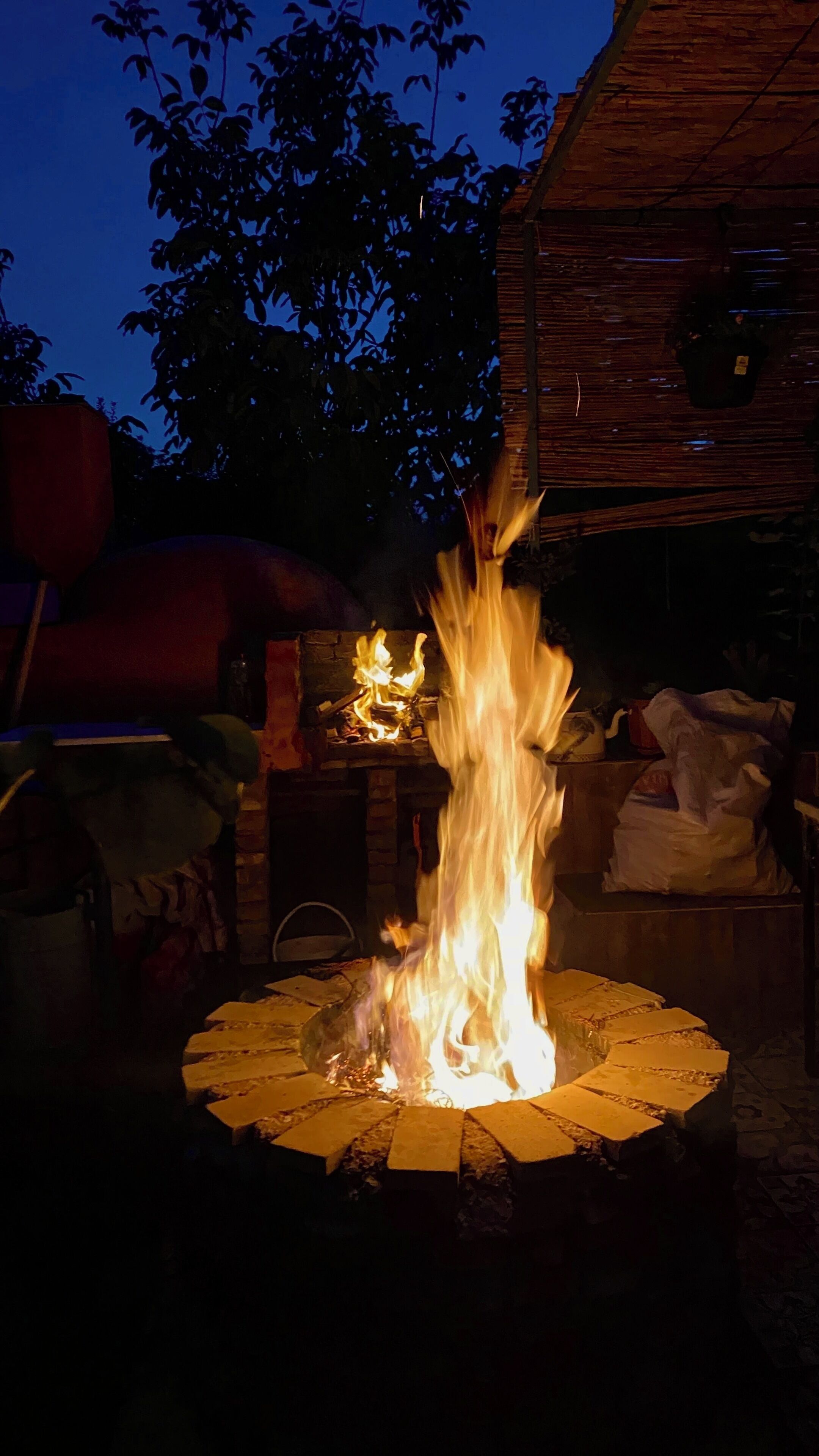 A fire pit with flames, surrounded by a brick fire ring, in a nighttime outdoor setting.