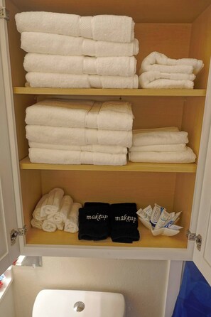 A bathroom with a white toilet, a shelf with folded towels, and a shelf with makeup items. - 4-bedroom 2-bathroom house VERY close to Lackland AFB BMT (San Antonio)