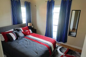 A bedroom with a bed, curtains, a nightstand, a lamp, a clock, a mirror, and a rug. - 4-bedroom 2-bathroom house VERY close to Lackland AFB BMT (San Antonio)