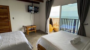 Una habitació d'hotel amb dos llits, un televisor fixat a la paret, una taula de fusta petita i un balcó amb vistes al mar.