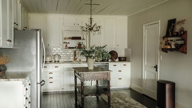 Une cuisine avec des meubles blancs, une table en bois et un lustre.