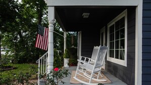 Une véranda avec un fauteuil à bascule, un drapeau américain et une plante en pot.