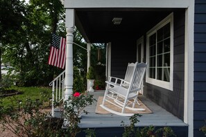Eine Veranda mit einem Schaukelstuhl, einer amerikanischen Flagge und einem Blumentopf.