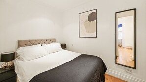 Ein Schlafzimmer mit Bett, Nachttisch, Wandlampe und Spiegel.