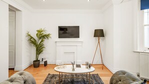 Ein Wohnzimmer mit rundem Couchtisch, einer Topfpflanze, einem Flachbildfernseher, einer Stehlampe und einem Kamin.
