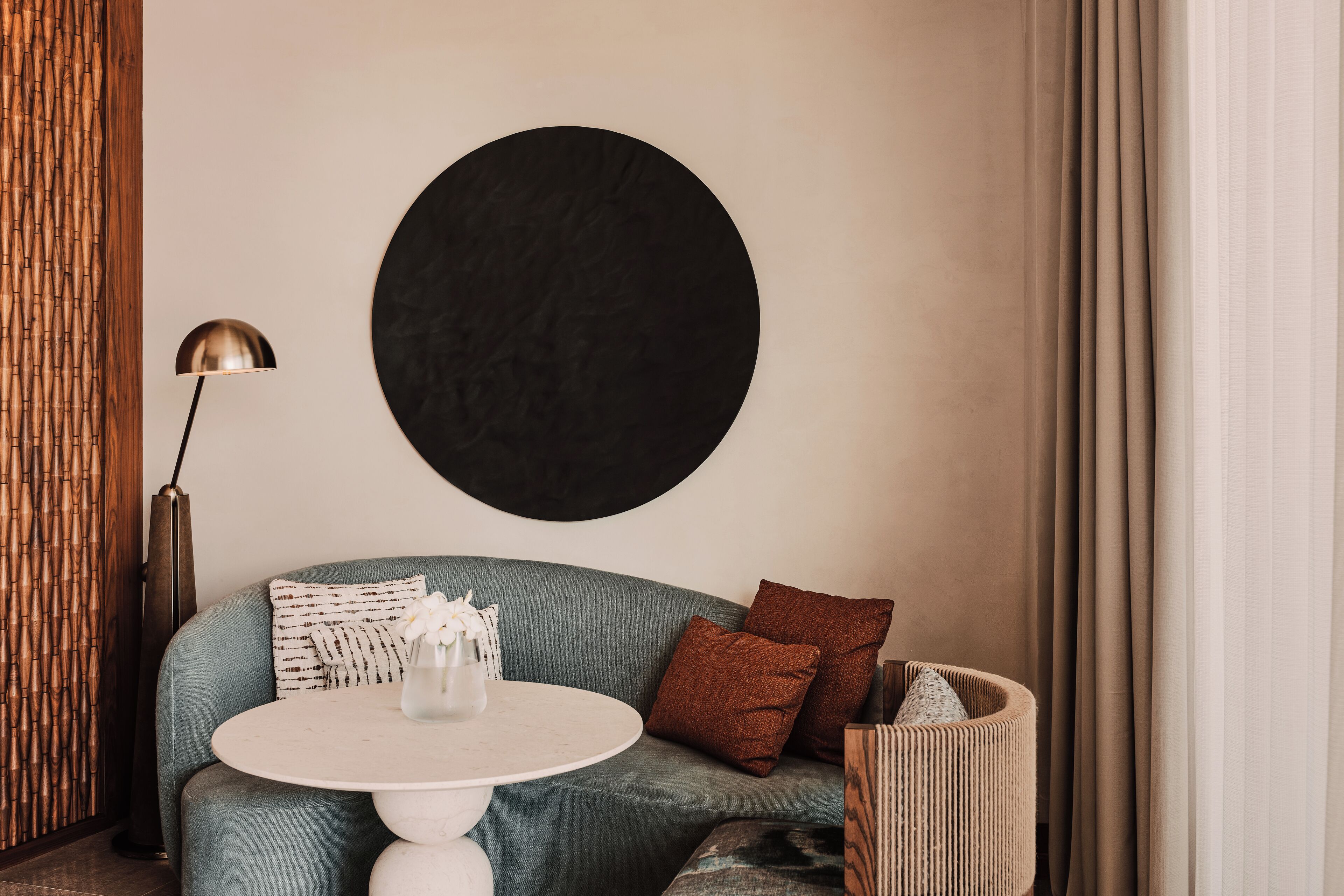 A modern living room with a sofa, a round table, a floor lamp, and a large black wall art piece.