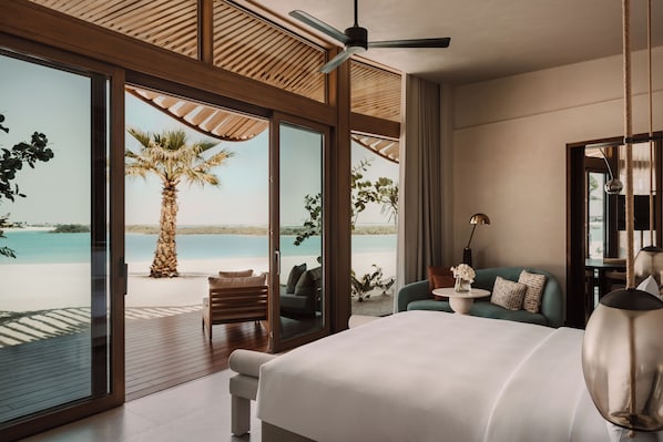 A bedroom with a large bed, a ceiling fan, a view of the beach, and a palm tree. - Miraval The Red Sea, Adults Only, All Inclusive Resort (Umluj)