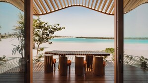An open wooden structure with a table and chairs facing a beach.