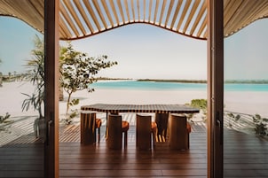 Estructura de madera abierta con una mesa y sillas frente a una playa.