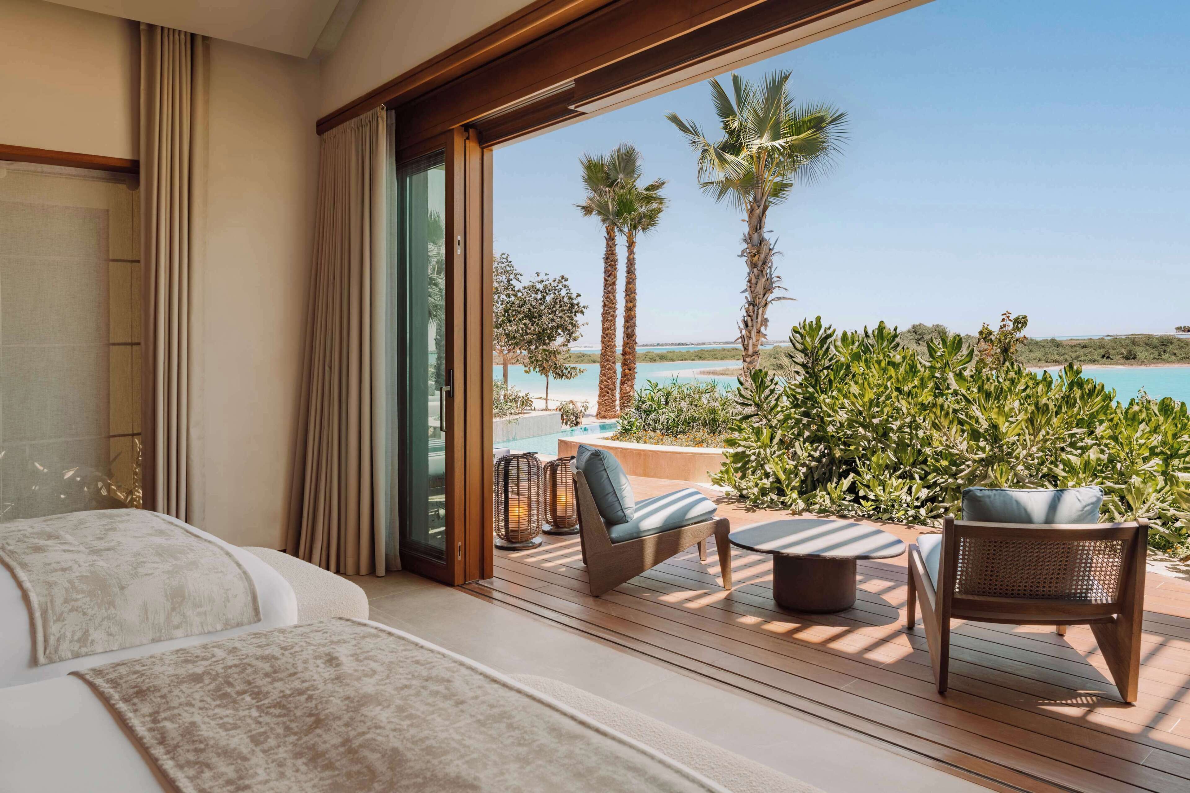 A balcony with a view of a pool and palm trees, furnished with a sofa, chairs, and a table.