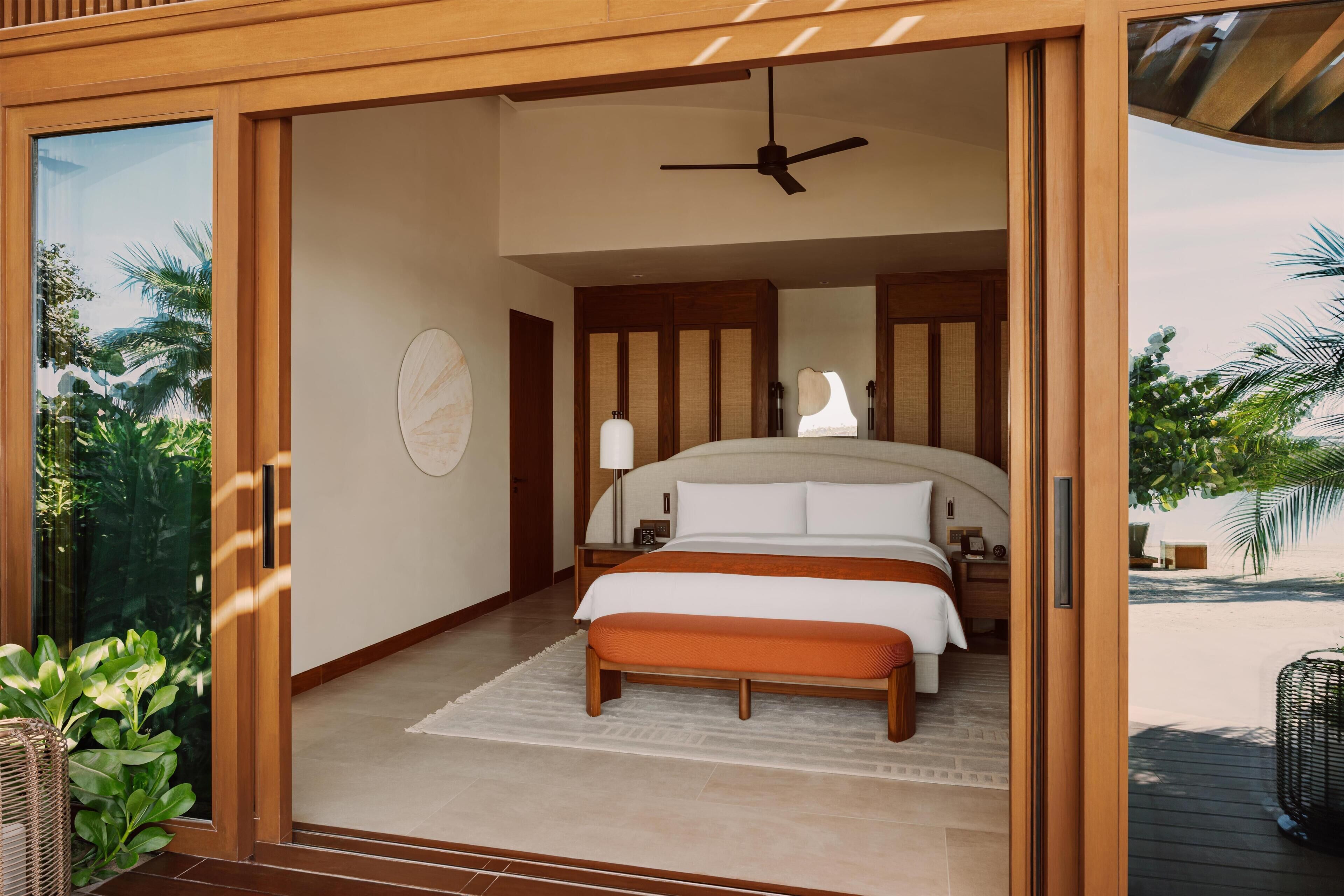 A bedroom with a bed, bedside tables, a ceiling fan, and a view of the outdoors.