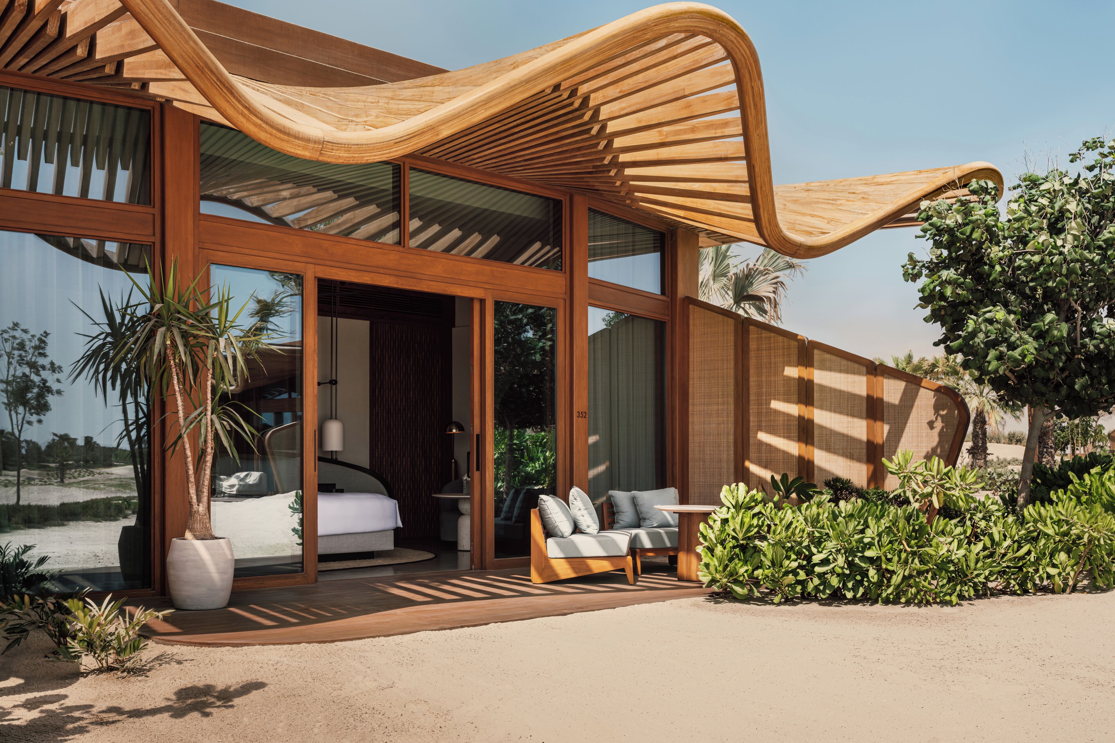 Una casa moderna con amplios ventanales, una estructura de madera curva, un sofá y una planta en maceta.