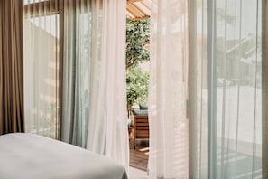 A room with a bed, sheer curtains, and a view of an outdoor seating area with a table and chairs. - Miraval The Red Sea, Adults Only, All Inclusive Resort (Umluj)