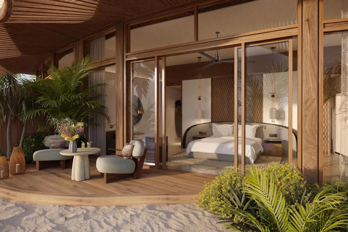 A modern, open-plan bedroom with a large bed, a seating area with a table, and a view through large glass doors.