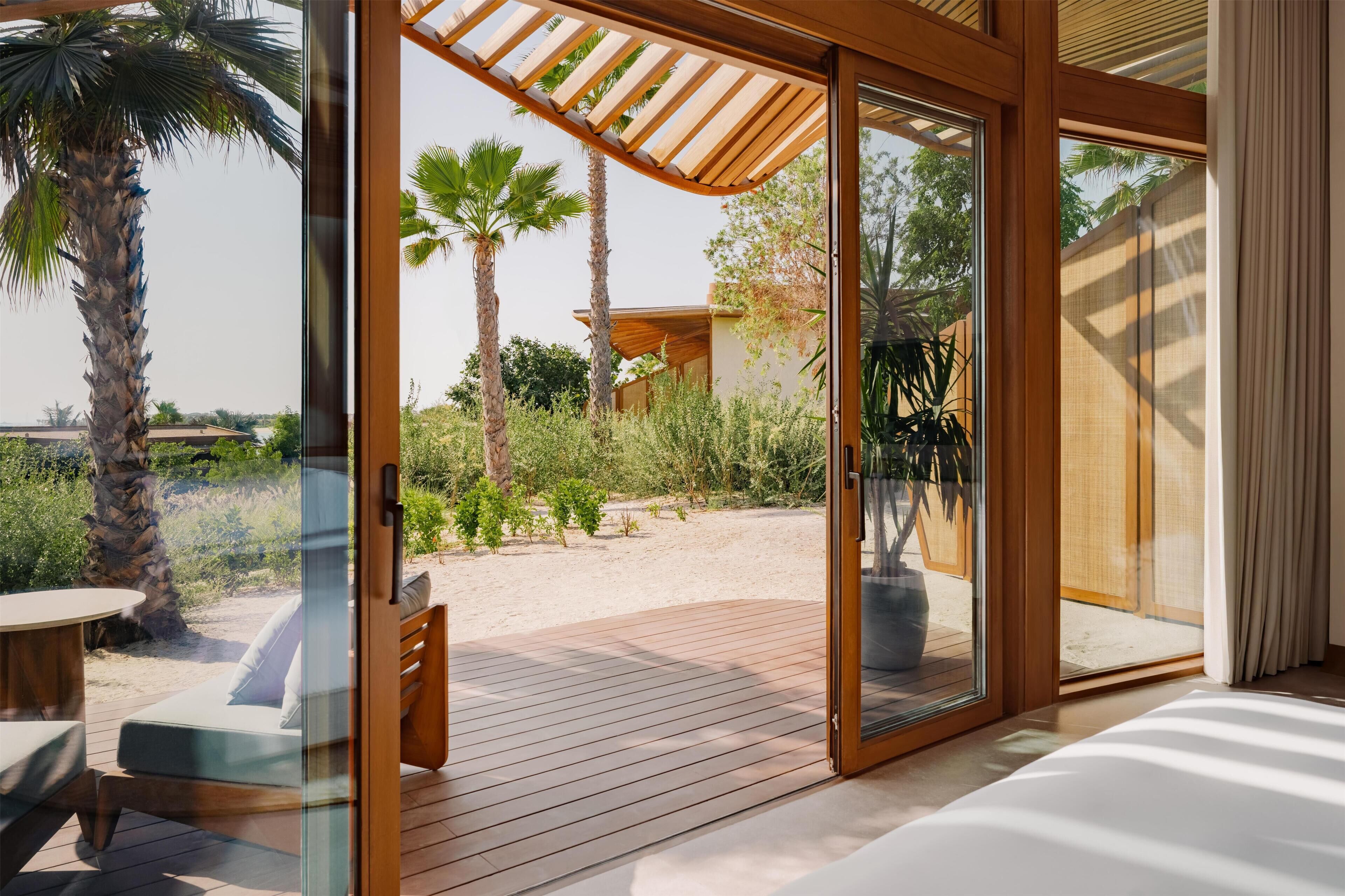Una habitación moderna con un amplio ventanal corredero que da a un espacio exterior con terraza de madera, una mesa y sillas.