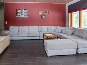 A modern living room with a grey sectional sofa, a small wooden coffee table, and a red accent wall with framed pictures.