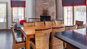 Een eetgedeelte met een stenen open haard, rieten stoelen en een grote houten tafel.