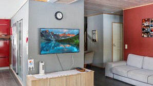 Een moderne woonkamer met een tv aan de muur, een houten kast, een rode wand en een grijze bank.