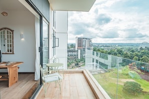 A balcony with a table and chairs, a view of a cityscape, and a glass railing.