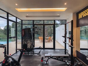A gym with exercise equipment, large windows, and a view of a pool and outdoor seating.